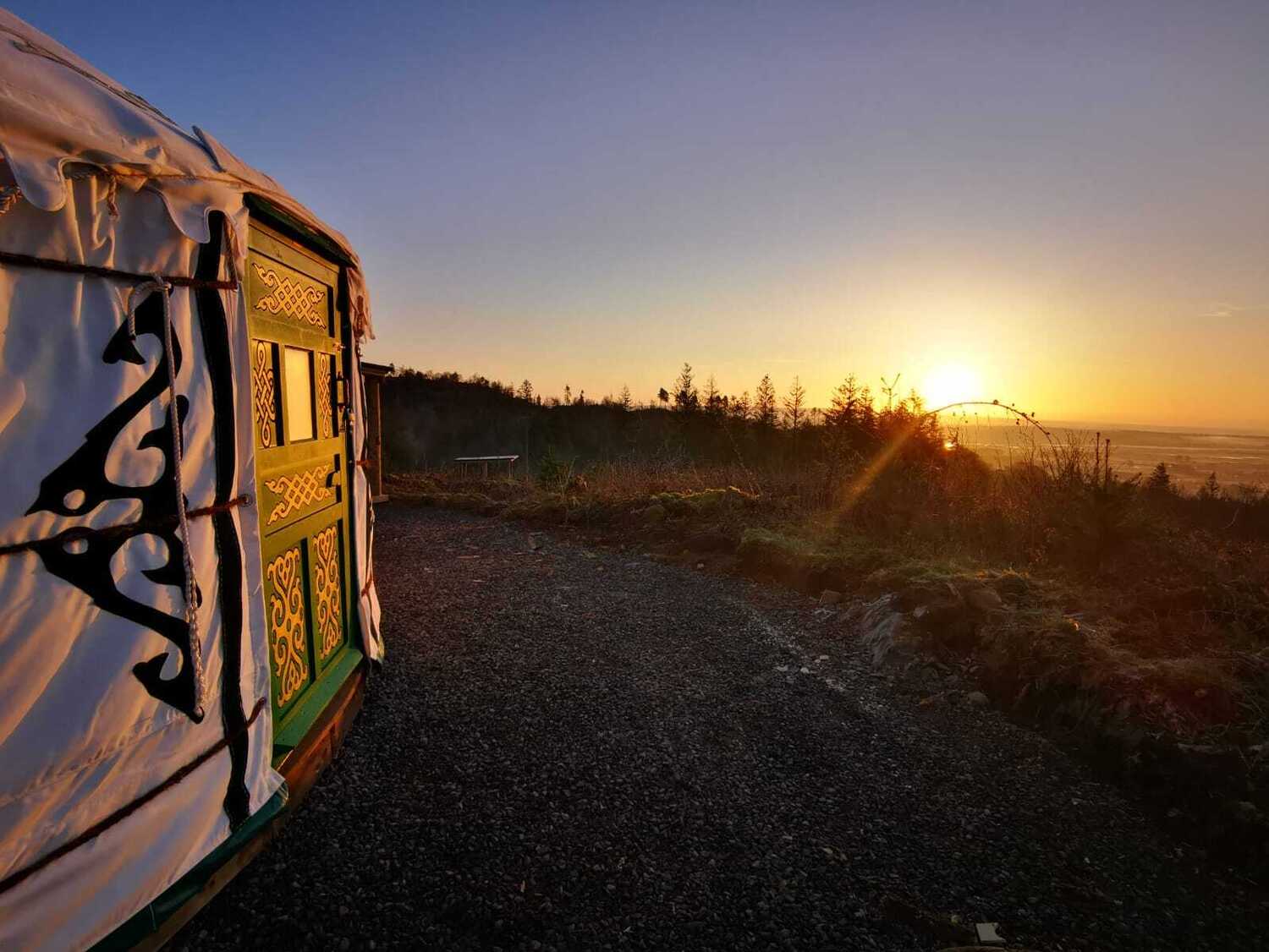 Glamping yurt named Wych Elm at sunrise. Ombre light is making the door glow deep orange
